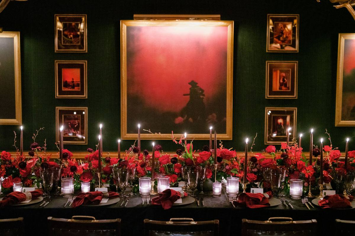 Rehearsal dinner table set against a dark green wall with framed art
